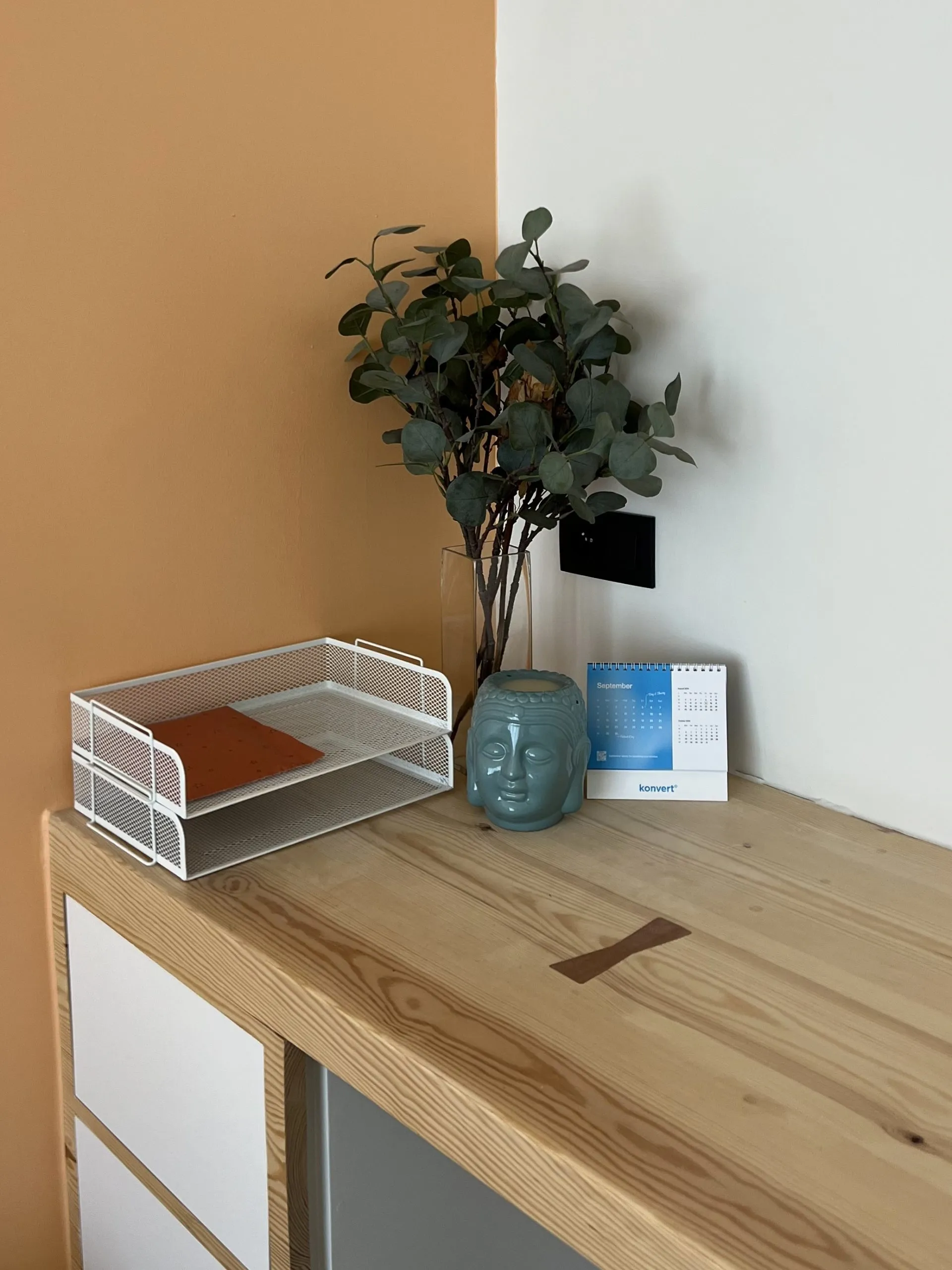 Bureau op maat in massief hout tegen een okerkleurige wand, met documentenbak en vaas op het blad