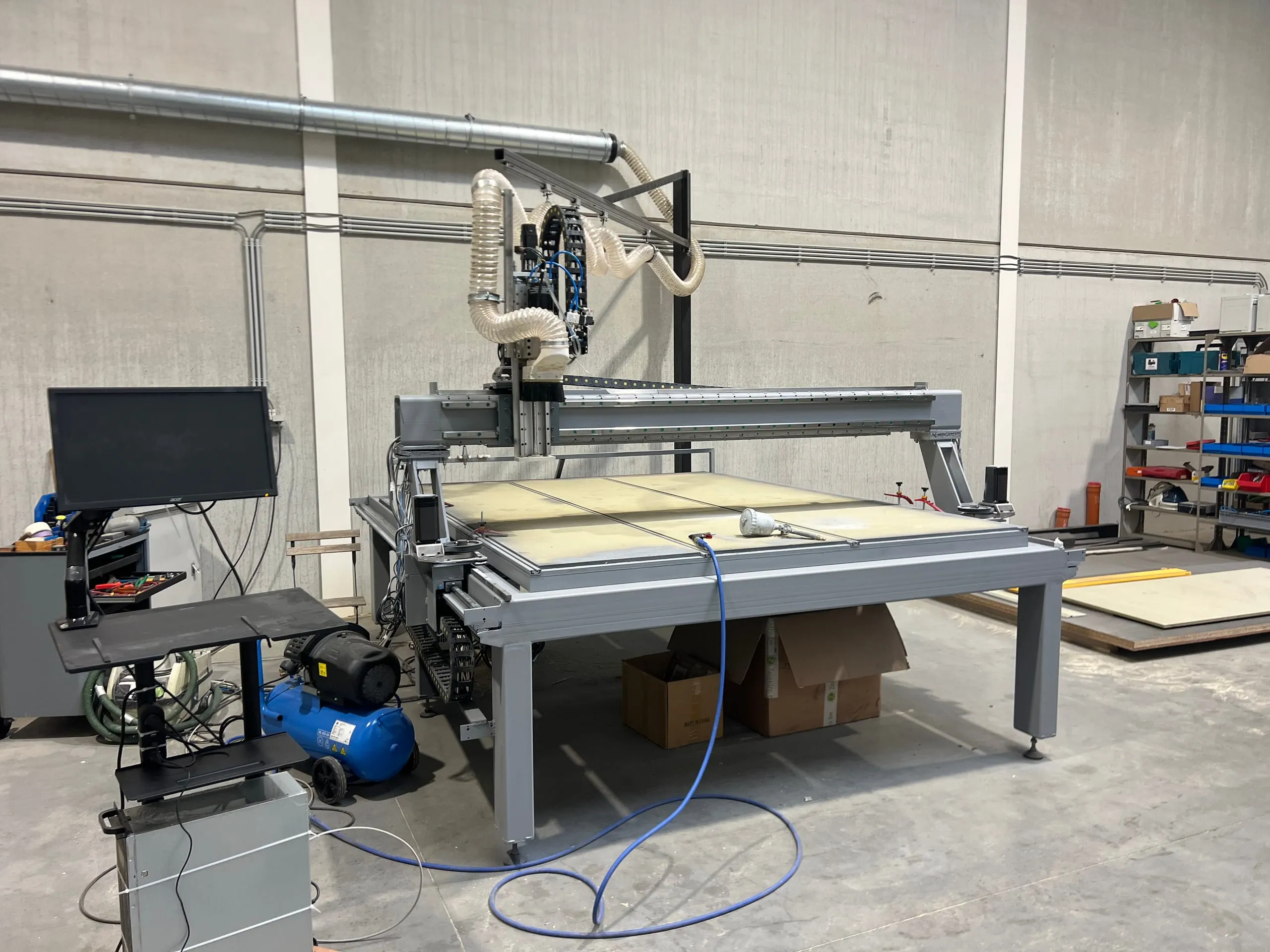 De computergestuurde freesmachine in het atelier, met het bedieningsscherm links en een freesbed op formaat van een volledige plaat